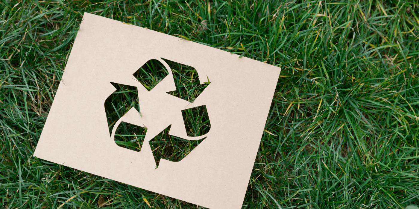 Symbole de recyclage découpé dans du carton, posé sur une pelouse verte. Représente l'engagement en faveur de l'environnement, l'écologie et le recyclage. Idéal pour les articles sur la durabilité et les pratiques écoresponsables.