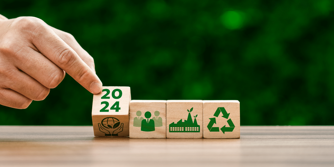 Main retournant un cube de bois marqué '2024', accompagné de symboles représentant la durabilité, le recyclage, et la responsabilité sociale. Image idéale pour aborder des sujets liés à la transition écologique, aux objectifs environnementaux pour 2024 et au développement durable.