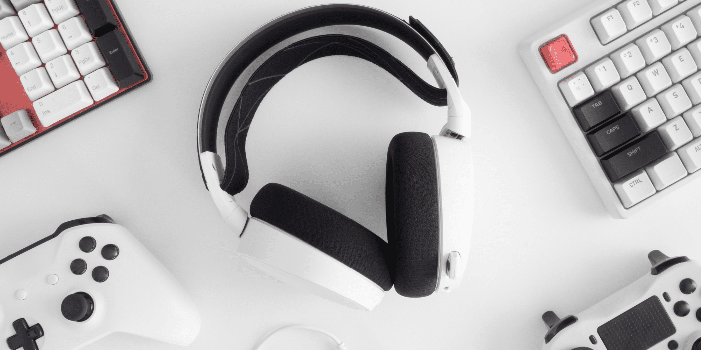 Un casque audio blanc entouré d'accessoires de jeu, comme des claviers et des manettes de jeu, sur une surface blanche. Parfait pour illustrer le thème des accessoires de gaming, des équipements audio de haute qualité, ou la tendance des gadgets gaming.