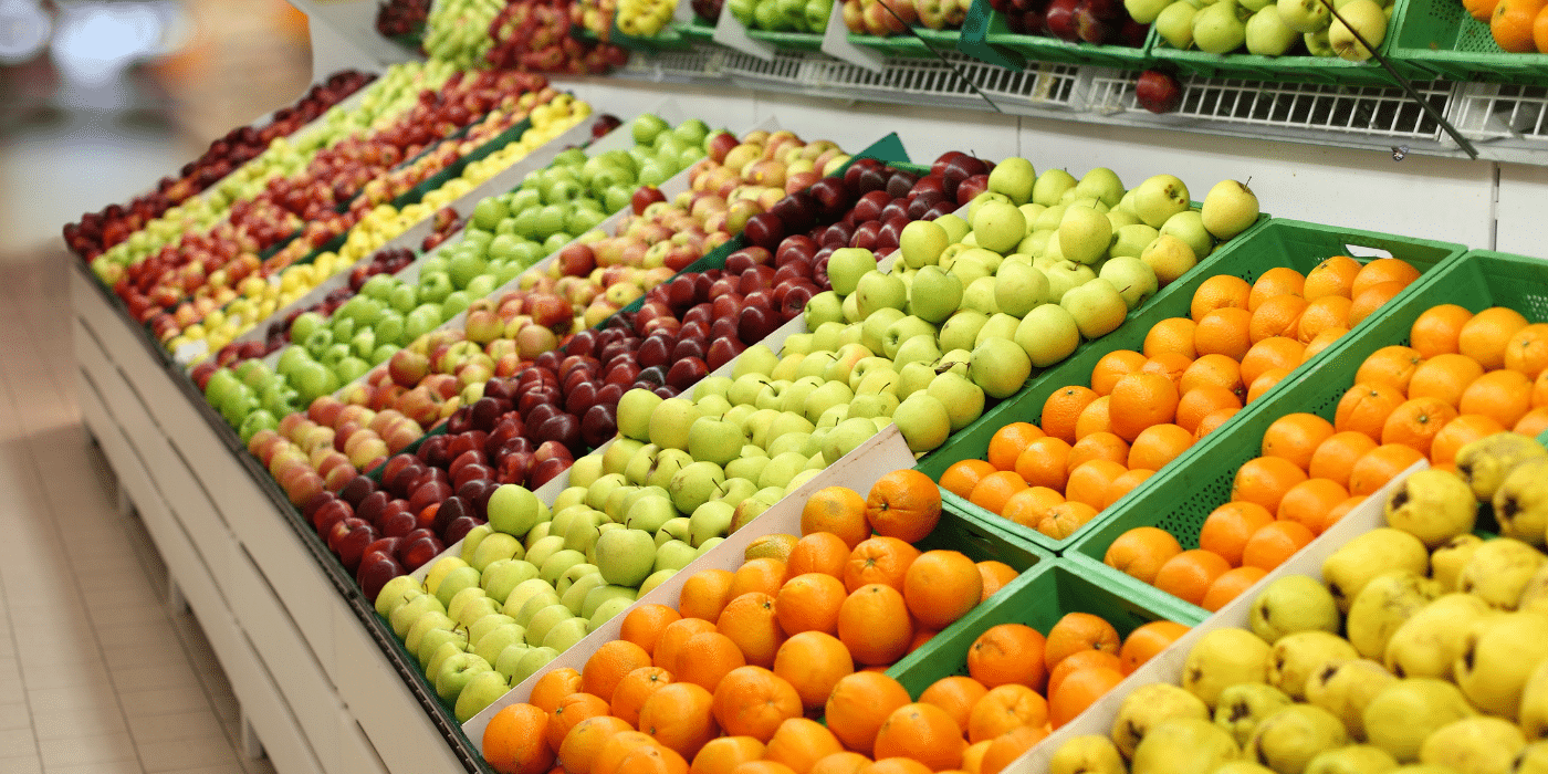 Alignement de fruits frais dans une épicerie Biocoop : Des rangées de pommes, oranges et autres fruits sont soigneusement alignées dans des cagettes vertes. Cette présentation ordonnée illustre l'engagement de Biocoop envers des produits frais, de saison, et souvent en vrac pour réduire les emballages superflus. En minimisant le plastique et en favorisant le zéro déchet, Biocoop offre aux consommateurs une alternative écologique pour faire leurs courses.