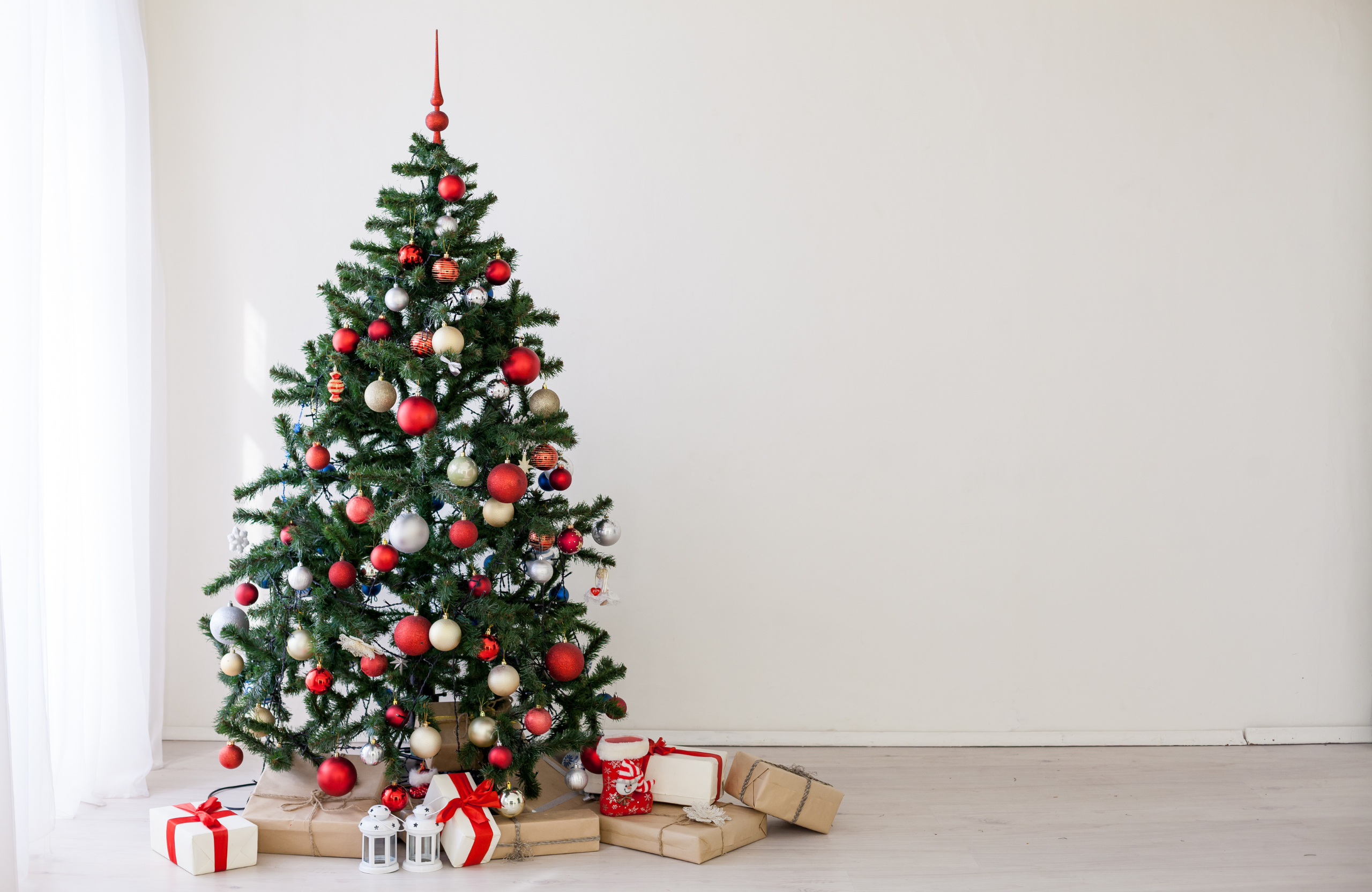 Sapin de Noël décoré avec des boules rouges et dorées, entouré de cadeaux, parfait pour illustrer des fêtes de fin d'année chaleureuses.