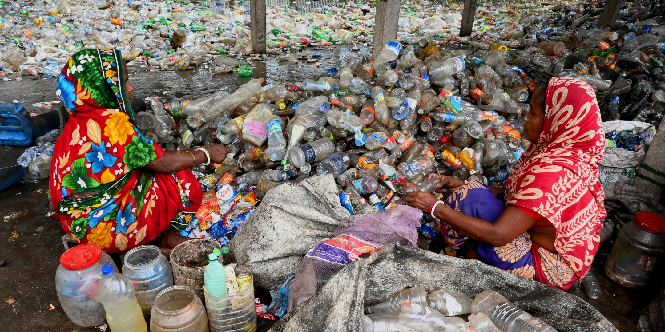 Deux femmes triant des bouteilles plastiques dans une décharge, mettant en lumière l'importance de l'effort humain dans le recyclage des déchets plastiques et les difficultés d'une gestion efficace du recyclage.