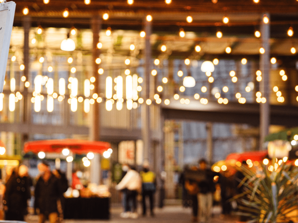 17. Marché ou événement en plein air, illuminé par des guirlandes lumineuses au crépuscule.