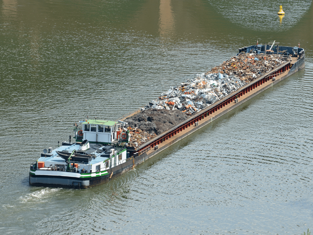 Barge naviguant sur un fleuve, chargée de déchets et matières recyclables.