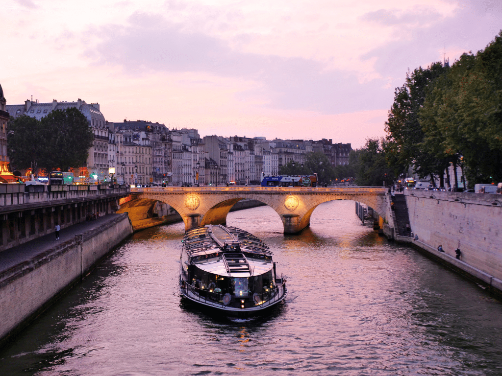 Le tri des déchets dans la Seine la déchetterie fluviale aide à réduire le transport routier des déchets Bateau de croisière touristique sur la Seine à Paris au coucher du soleil, avec un pont illuminé en arrière-plan.