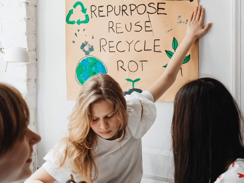 Deux femmes participent à un atelier écologique, devant une affiche avec les mots “Repurpose, Reuse, Recycle, Rot”.