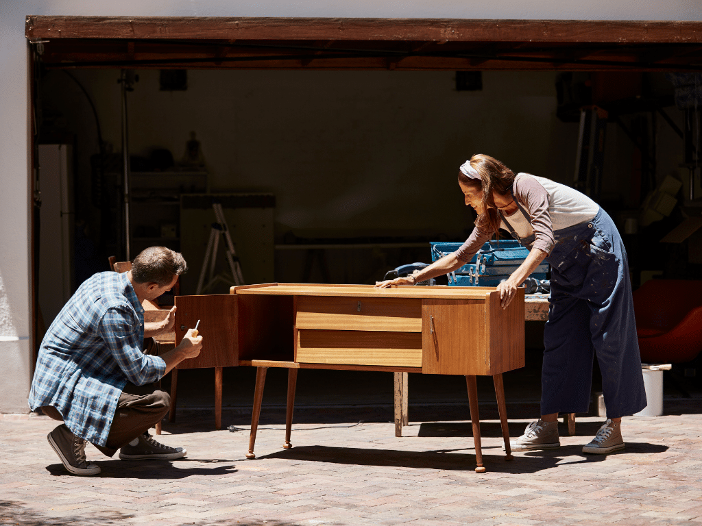 Deux personnes ponçant et réparant un meuble en bois dans un atelier, illustrant la réutilisation et la rénovation de mobilier de bureau