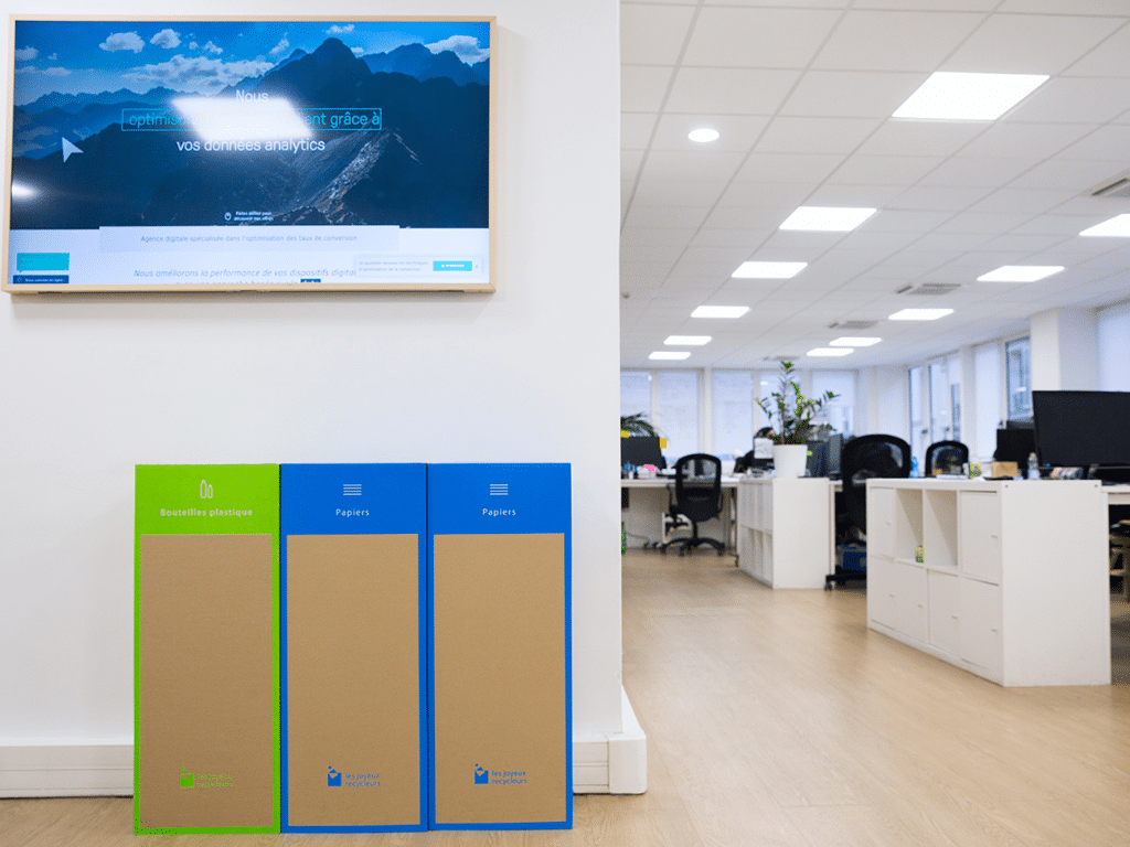 Bureau lumineux équipé de poubelles de tri colorées, illustrant une organisation de travail écoresponsable et le recyclage au quotidien.