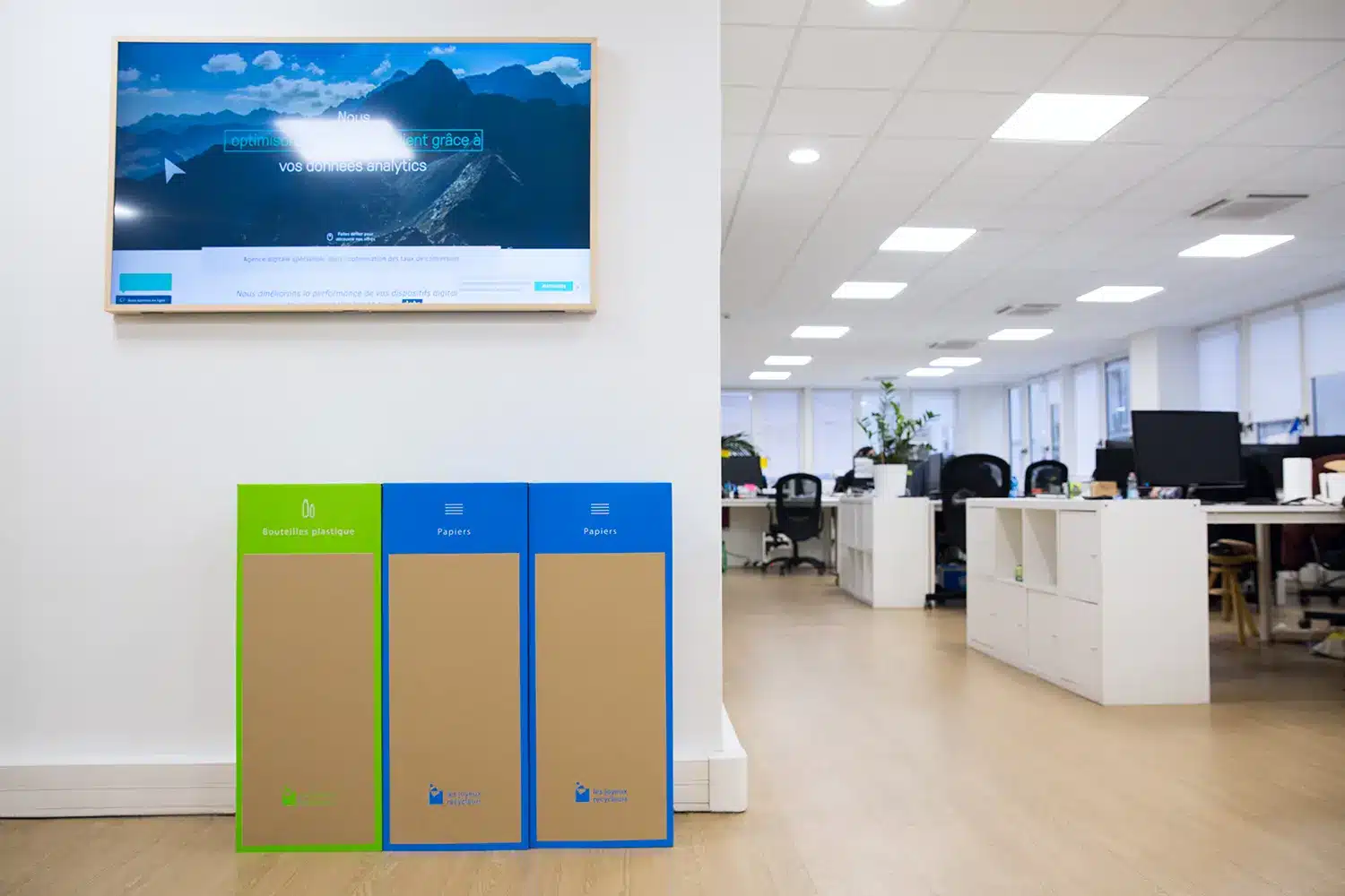 trois poubelles de tri papier et plastique dans un open space